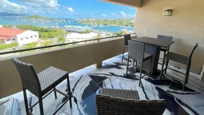 Un balcon avec vue sur un port de plaisance et des immeubles. On y trouve deux tables et quatre chaises en osier.