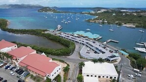 Vue aérienne d’une marina avec des bateaux, un parking et des bâtiments aux toits rouges.