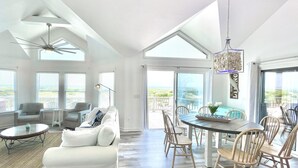 A spacious living room with a white sofa, dining table, and chairs, large windows, and a ceiling fan.