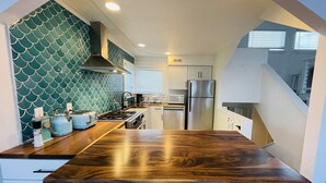 A compact kitchen with a wooden countertop, white cabinets, a stainless steel refrigerator, and a teal backsplash.