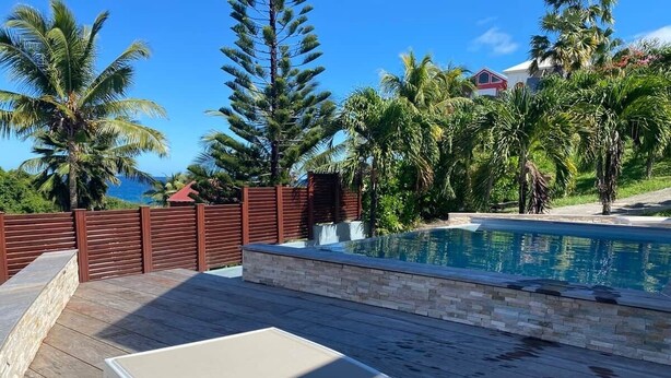 A pool area with a wooden deck, a lounge chair, and a stone wall.