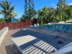 Un área de piscina con cubierta de madera, una silla de descanso y una pared de piedra.