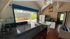 A modern kitchen with a large island, a dining area with a white table and chairs, and a wicker sofa.
