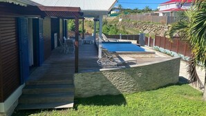 A pool area with a covered deck, lounge chairs, and a stone wall.