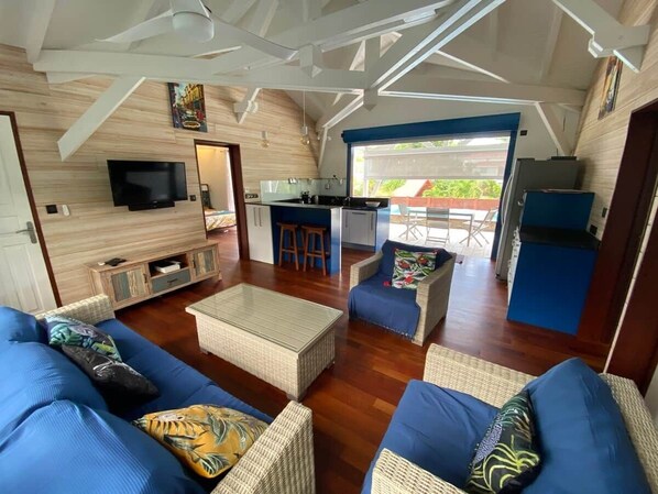 Amplia sala de estar con un conjunto de sofás, una mesa de centro y una cocina con televisor y taburetes de bar.