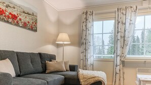 A modern living room with a grey sectional sofa, a floor lamp, and a window with patterned curtains. - Iso-karpalo a by Interhome (Kuusamo)