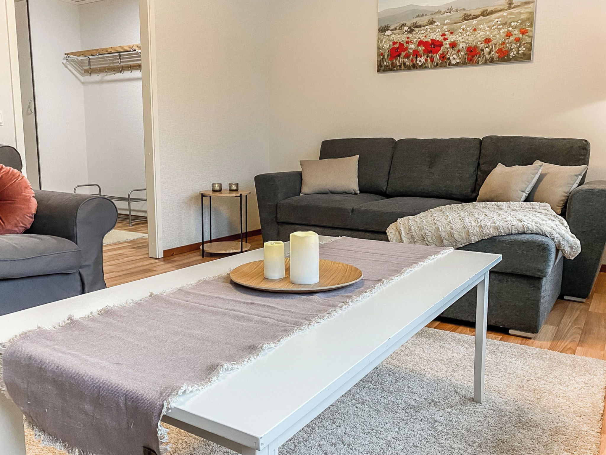 A modern living room with a grey sofa, a white bench, and a painting of flowers on the wall.