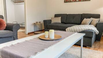 A modern living room with a grey sofa, a white bench, and a painting of flowers on the wall.