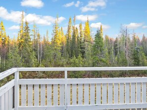 A wooden deck with a railing overlooking a forest of trees with yellow foliage.