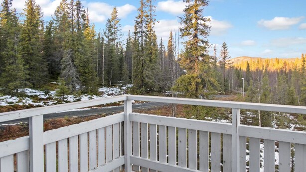 A wooden deck with a white railing overlooking a forested area with snow patches. - Iso-karpalo a by Interhome (Kuusamo)