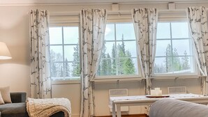A cozy room with a sofa, a table, and a view of trees through large windows. - Iso-karpalo a by Interhome (Kuusamo)
