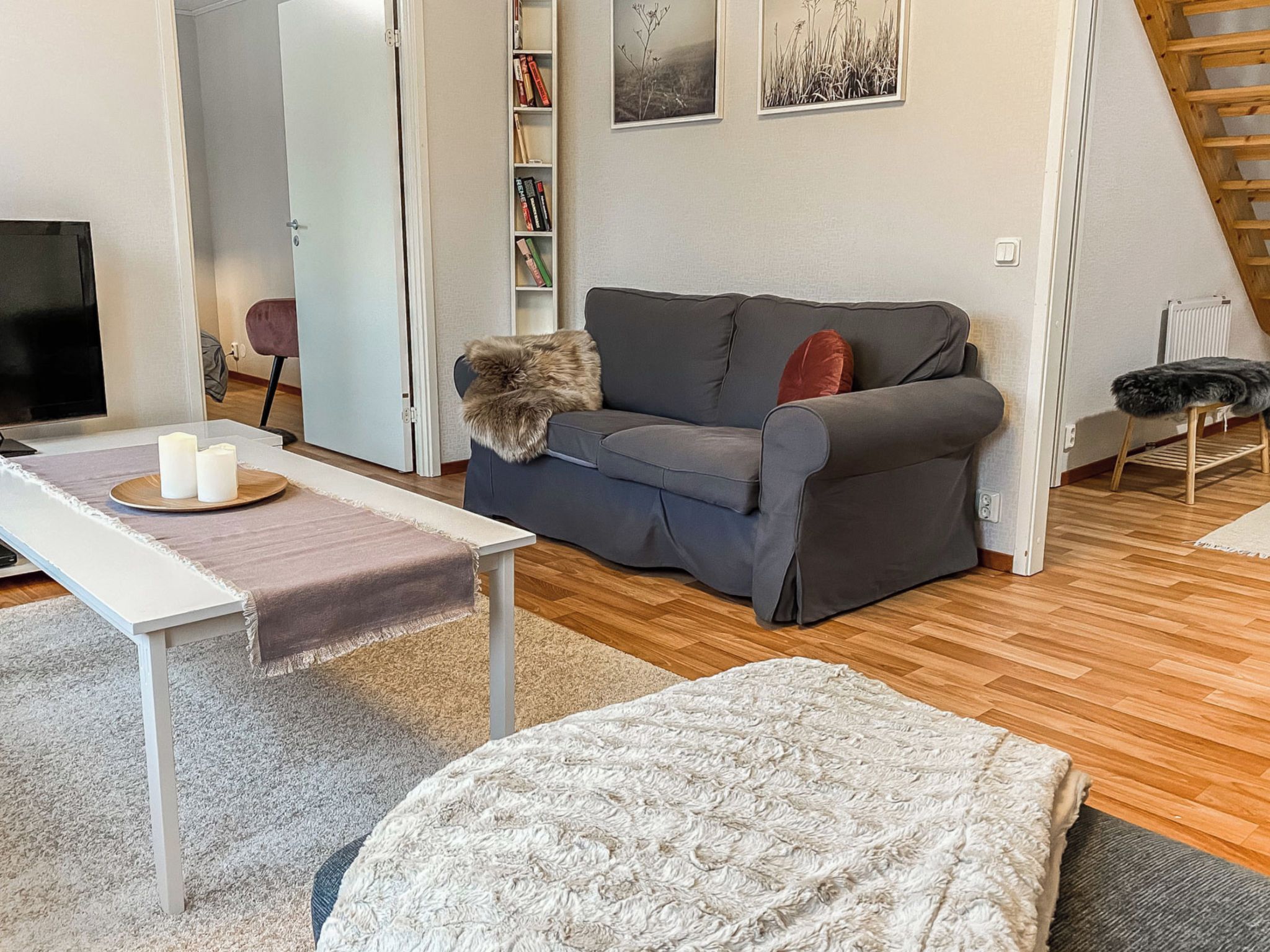 A living room with a grey sofa, a white coffee table, a small rug, and a bookshelf with books.
