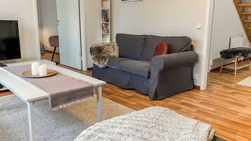 A living room with a grey sofa, a white coffee table, a small rug, and a bookshelf with books.