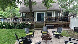 Eine Terrasse mit vier Adirondack-Stühlen, einer Feuerstelle und einem überdachten Deck.