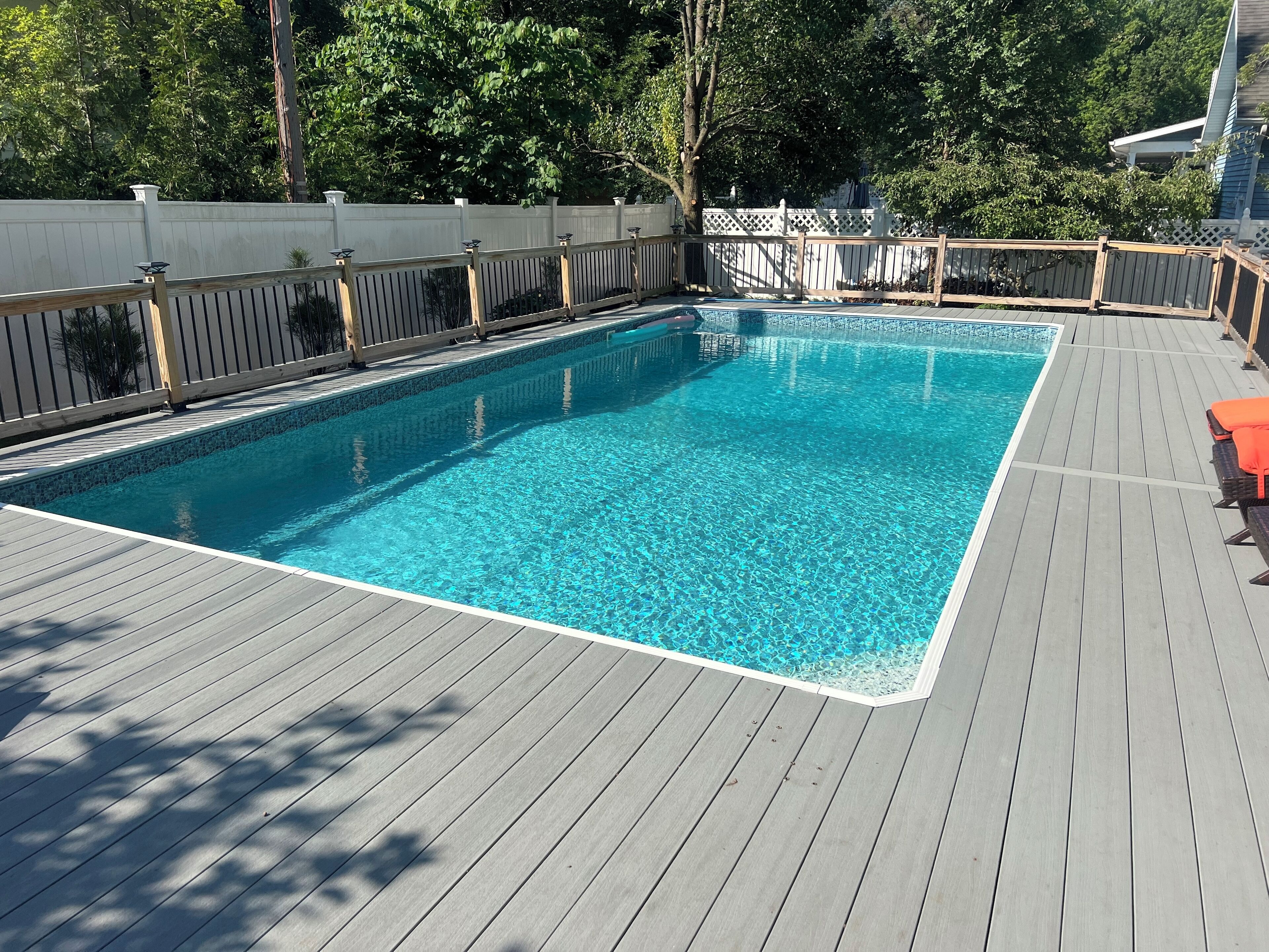 A rectangular swimming pool with a wooden deck surrounding it.