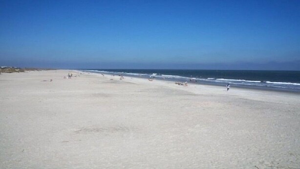 Een breed zandstrand met een helderblauwe lucht en een rustige zee.