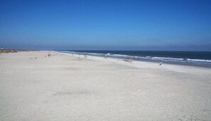A wide sandy beach with a clear blue sky and calm sea.