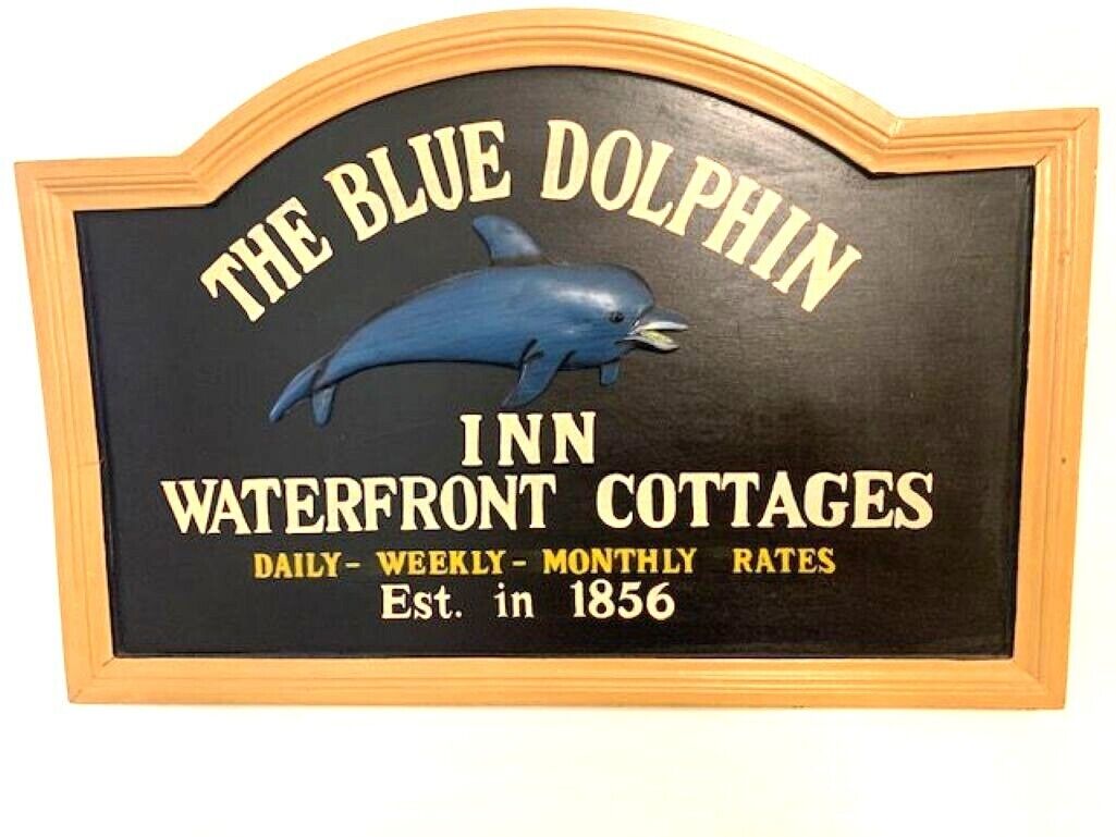 A sign for The Blue Dolphin Inn Waterfront Cottages with a dolphin graphic, indicating it was established in 1856.