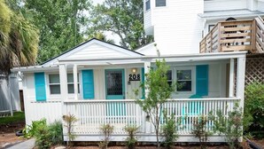 Een wit huis met nummer 208, een veranda met blauwe luiken en een kleine boom in de voortuin.