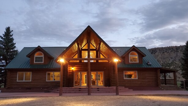 A log cabin with a central entrance, two side wings, and a metal roof. - Secluded luxury lodge that sleeps 34 in beds (Price)