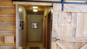 A wooden interior with a central hallway leading to a door with a cross-brace design. - Secluded luxury lodge that sleeps 34 in beds (Price)