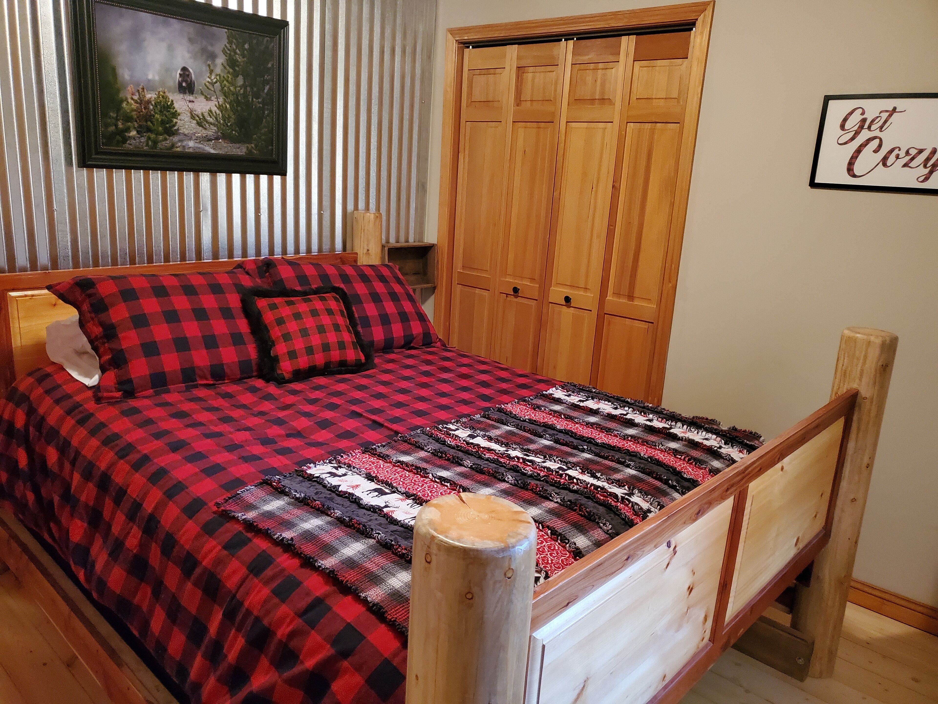 A bedroom with a checkered bedspread, a wooden wardrobe, and a framed picture on the wall.