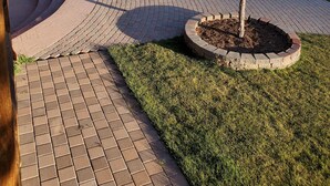 A landscaped outdoor area with a curved brick pathway, a small tree in a circular planter, and a tall evergreen tree. - Secluded luxury lodge that sleeps 34 in beds (Price)