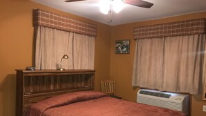 A bedroom with two beds, a ceiling fan, an air conditioner, and plaid curtains. - Catskills Adventures (Roscoe)