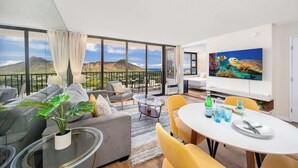 A modern living room with a large window, a dining area, and a TV. - 34th floor lanai w/ pool & hot tub access (Honolulu)