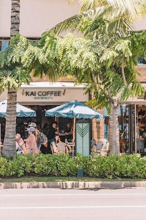 Una cafetería llamada 'KAI COFFEE' con terraza y palmeras.