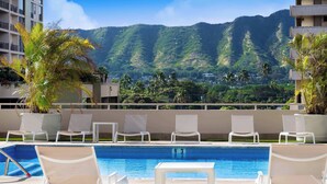 A poolside area with lounge chairs and a view of a mountainous landscape.