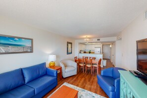 Ein Wohnzimmer mit zwei blauen Sofas, einem Couchtisch, einem Fernseher und einem Essbereich mit Tisch und Stühlen.