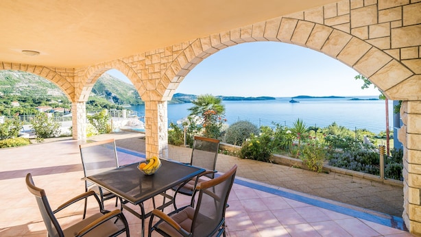 A covered outdoor seating area with a table and chairs, overlooking a body of water and greenery. - Apartment Blue Chill- Comfort Studio Apartment (Mlini)
