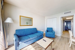 Una sala de estar con un sofá azul, una mesita, una silla, una lámpara y un espejo en la pared.