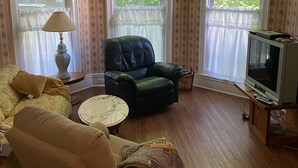 Un salon comprenant un fauteuil en cuir, un canapé, une petite table ronde et un téléviseur posé sur un meuble en bois.