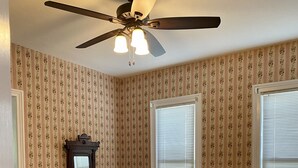 Une salle à manger avec une table en bois, un papier peint à motifs floraux et un ventilateur de plafond.