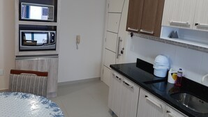 A kitchen with a microwave, oven, and a sink. There are cabinets and a countertop with a few items on it.