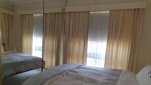 Een hotelkamer met twee bedden, beige gordijnen en uitzicht op de omgeving.