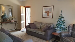 Een woonkamer met een gestreept bankje, een klein rond tafeltje, een kerstboom en een spiegel met een decoratieve lijst.