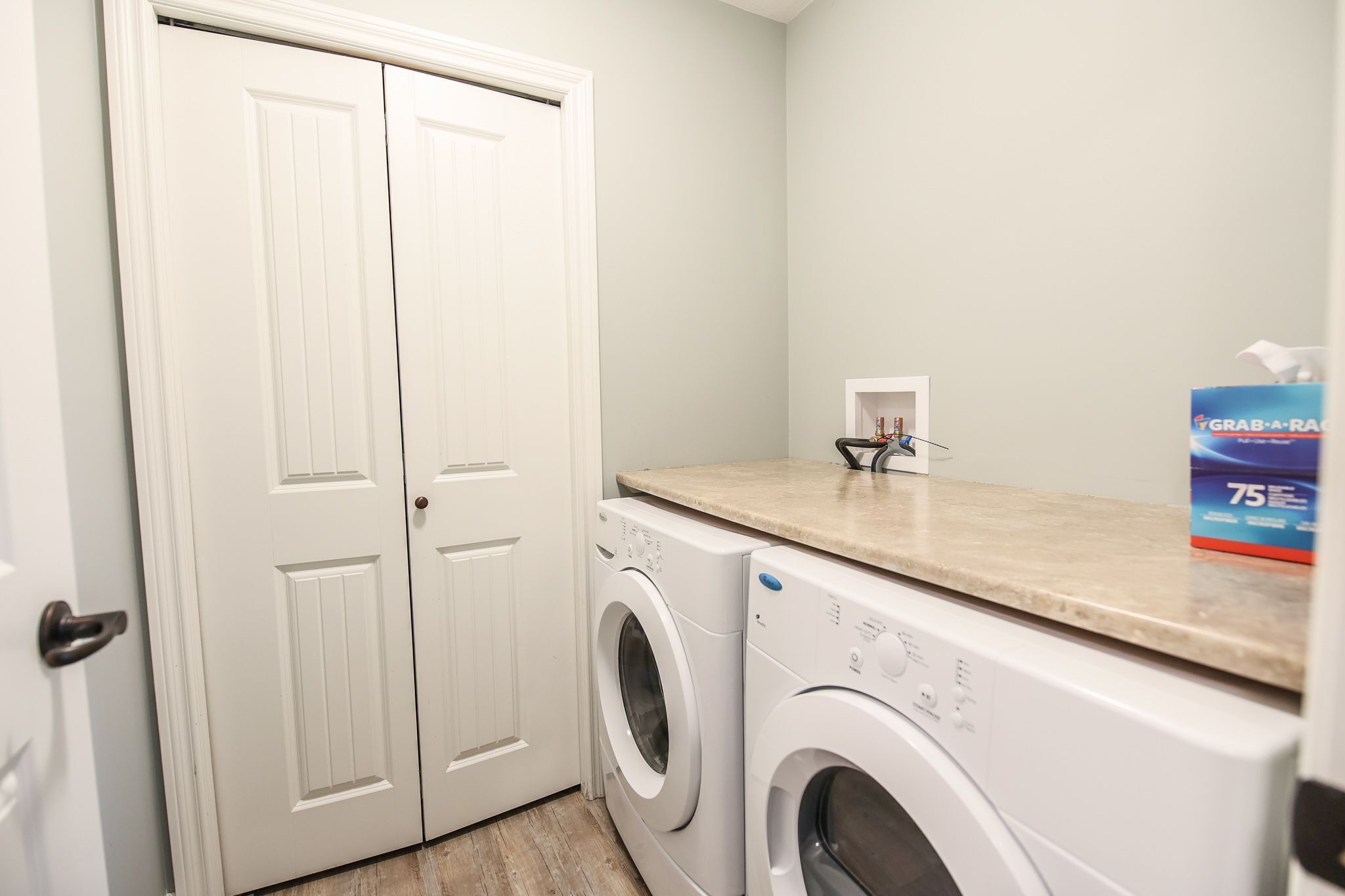 A laundry room with two white front-loading washing machines, a beige countertop, and a box of laundry detergent.