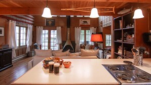 L’intérieur chaleureux d’un chalet comprend une table à manger, deux chaises, une cheminée, un canapé et un coin cuisine avec un poêle.