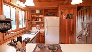 Une cuisine rustique aménagée dans une cabane en bois, avec un poêle, un évier, un réfrigérateur et des étagères remplies d’ustensiles de cuisine.