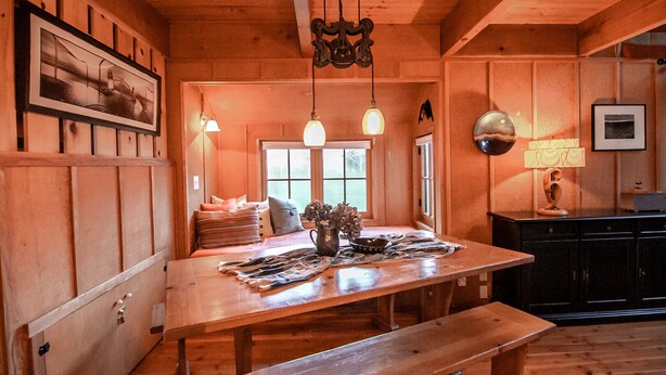 Un intérieur en bois avec une table à manger, des bancs et des luminaires suspendus.