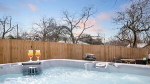 Un bain à remous avec deux verres d’une boisson rouge et jaune, entouré d’une clôture en bois et d’arbres sans feuilles.