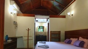 Un dormitorio con cama, cabecera de madera, mesita de noche, espejo y ventana con vista a la vegetación.