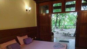Una habitación con cama, almohadas y vistas a un bosque a través de puertas abiertas.