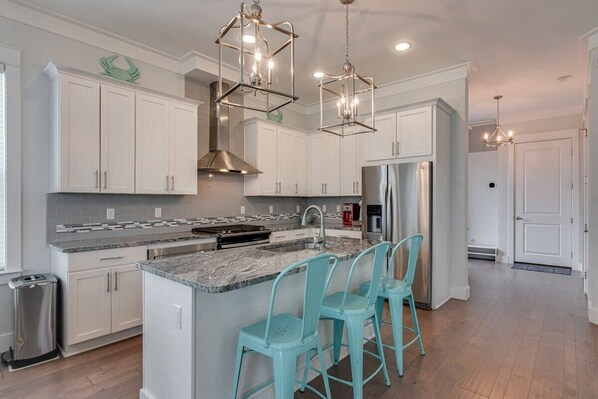 A modern kitchen with white cabinets, a central island with bar stools, stainless steel appliances, and pendant lighting.
