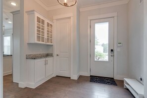A spacious entryway with a wooden floor, a white door, and a built-in cabinet with glass doors.