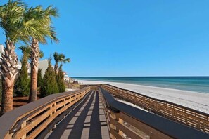 Une promenade en bois menant à une plage bordée de palmiers, sous un ciel bleu et dégagé.