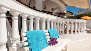 Eine weiße Bank mit zwei blauen Handtüchern und lila Blumen vor einer weißen Balustrade mit Bögen.